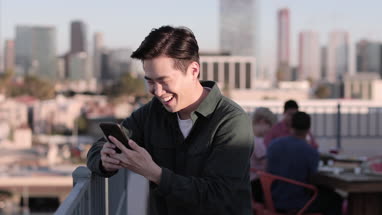 Young adult male messaging friend from a rooftop party