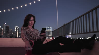 Young adult female looking at smartphone on a rooftop at night