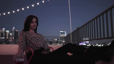 Young adult female looking at smartphone on a rooftop at night