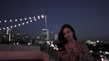 Young adult female looking at smartphone on a rooftop at night