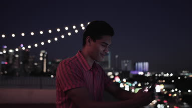 Young adult male looking at smartphone on a rooftop at night