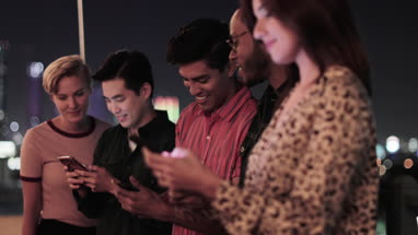 Group of friends on smartphones outdoors in city at night