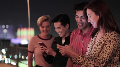 Group of friends on smartphones outdoors in city at night