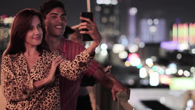 Young adult couple taking selfie with city skyline at night