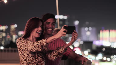 Young adult couple taking selfie with city skyline at night