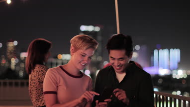 Young adult couple taking selfie with city skyline at night