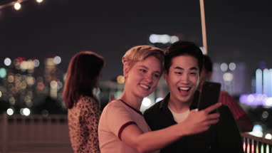 Young adult couple taking selfie with city skyline at night