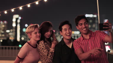 Group of friends taking selfies with city skyline at night