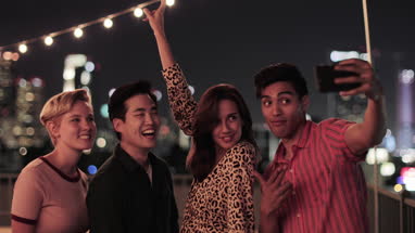 Group of friends taking selfies with city skyline at night
