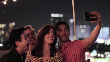Group of friends taking selfies with city skyline at night