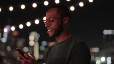 Young adult male messaging friend from a rooftop party