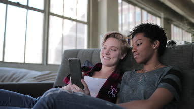 Female couple relaxing on sofa looking at smartphone