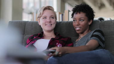 Female couple relaxing on sofa watching home entertainment