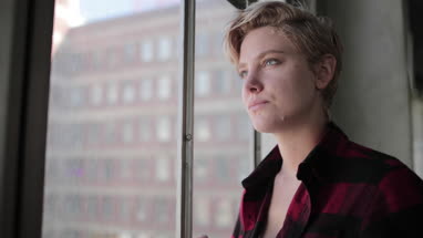 Young female looking out of window in loft apartment thinking