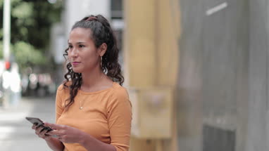 Portrait of hispanic young adult female using smartphone on busy city street
