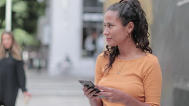 Portrait of hispanic young adult female using smartphone on busy city street